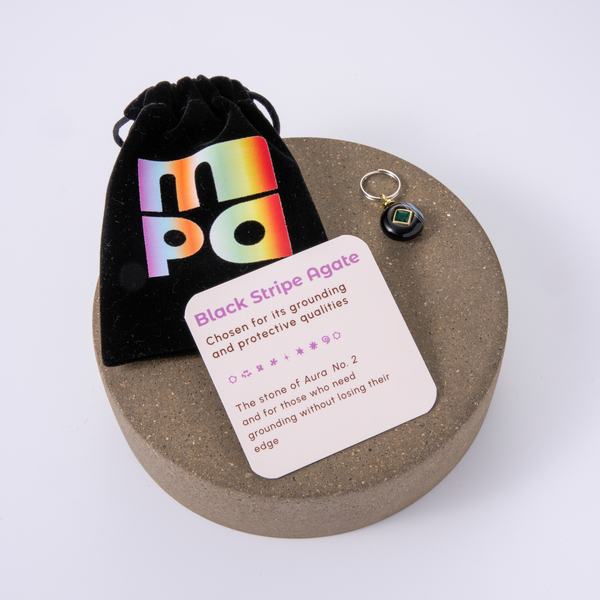 Black Stripe Agate crystal charm with a black velvet pouch and an informational card, displayed on a round wooden tray against a white background.