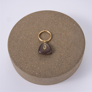 A black agate charm with a gold split ring, displayed on a round stone pedestal.