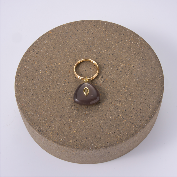 A black agate charm with a gold split ring, displayed on a round stone pedestal.