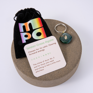 Water Grass Agate crystal charm with a black velvet pouch and an informational card, displayed on a round wooden tray against a white background.