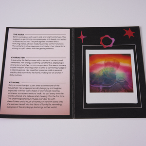 A printed booklet or card set photographed on a light gray background. The left page is white with black text and headings, and the right page is black with a colorful rectangular illustration showing a sunset-like gradient and pink star-like shapes.