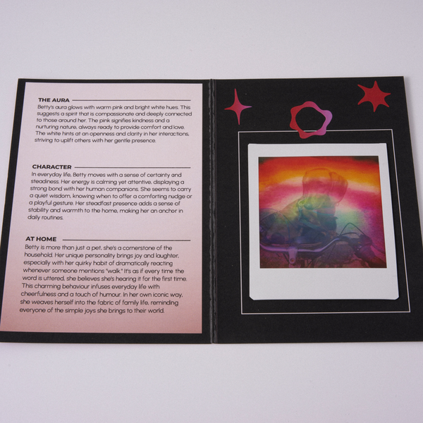 A printed booklet or card set photographed on a light gray background. The left page is white with black text and headings, and the right page is black with a colorful rectangular illustration showing a sunset-like gradient and pink star-like shapes.