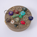 A collection of colorful stone charms with gold-tone rings, displayed on a round textured brown stand against a light gray background.