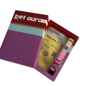 A pet collar set in an open branded box labeled 'my pet aura'. The collar is pink, yellow, blue with a patterned design and silver hardware, shown alongside printed inserts and packaging on a plain white background.