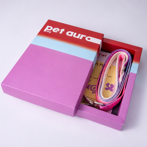 A pink and red 'pet aura' branded gift box shown open on a white background, revealing a pink and purple pet lead and a yellow card insert.