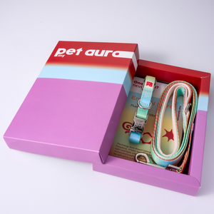 A pet accessory set in a purple and red box, featuring a light rainbow lead and collar with a metal clasp and a red-and-white 'pet aura' box lid.