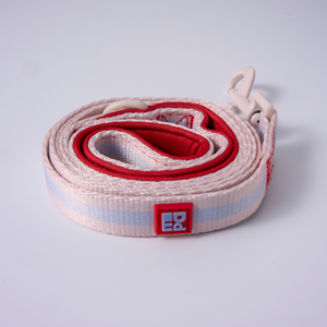 A coiled white dog leash with a red inner lining, a metal snap hook clasp, and a small square brand patch on a light gray background.