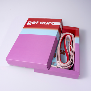 A pink and red 'pet aura' branded gift box shown open on a white background, revealing a white and red pet lead and a blue card insert.