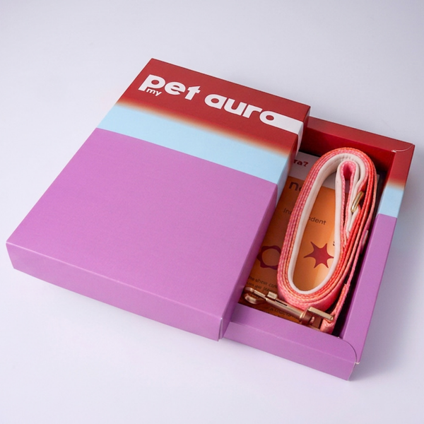 A pet accessory gift set in a pink and red box with the brand name 'pet aura' visible on the lid. The set includes a pink and white lead with a red star detail and a small booklet.